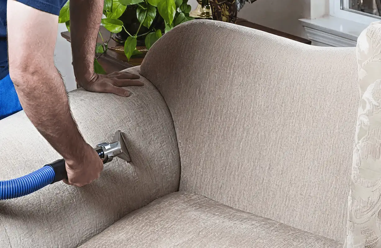 Professional upholstery cleaner deep-cleaning a fabric sofa with a handheld extraction tool and hose, San Antonio, TX.